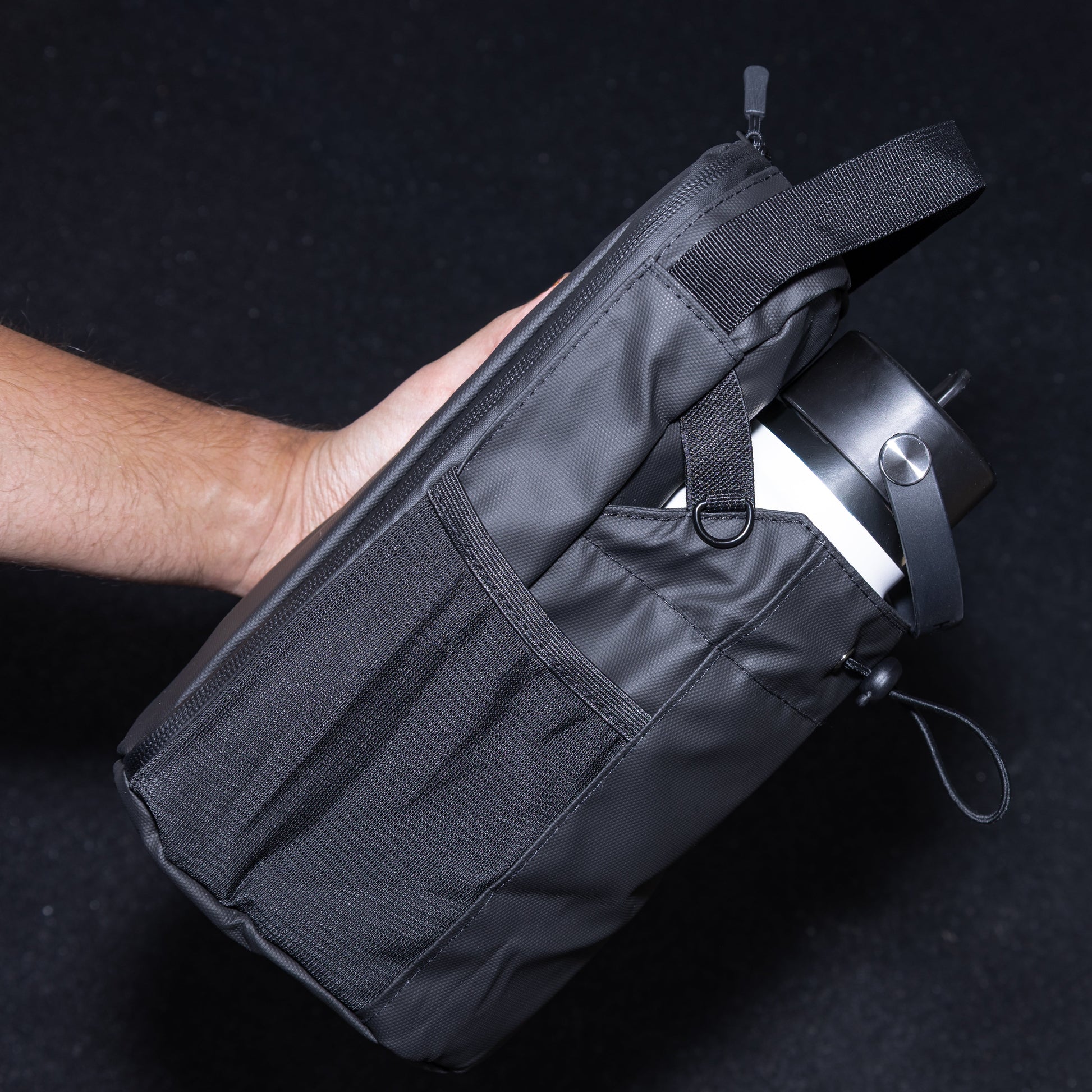 Black tactical pouch held by a person against a black gym floor as background